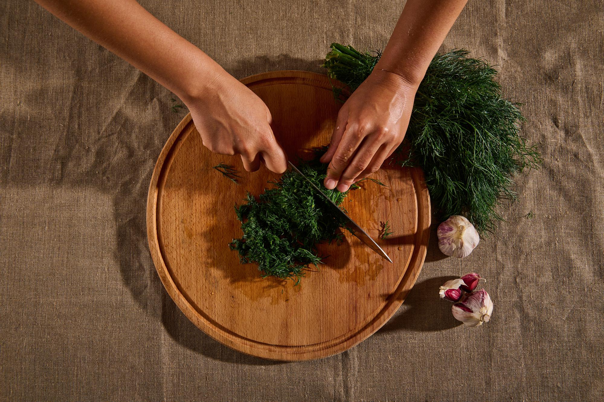 close-up of hands preparing plated appetizer with herbs